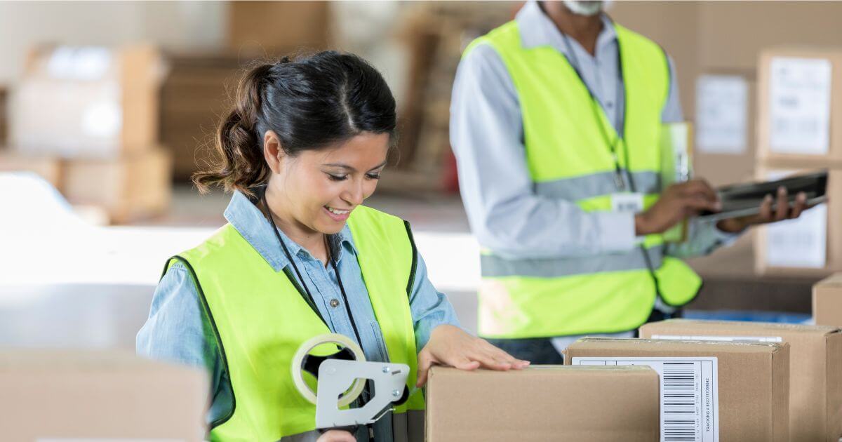 smiling warehouse worker taping box closed