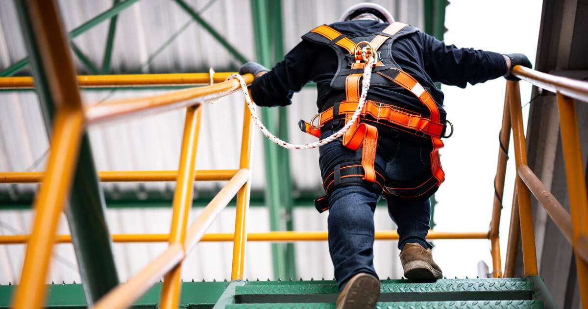 Worker wearing fall protection harness climbing industrial stairs at a job site